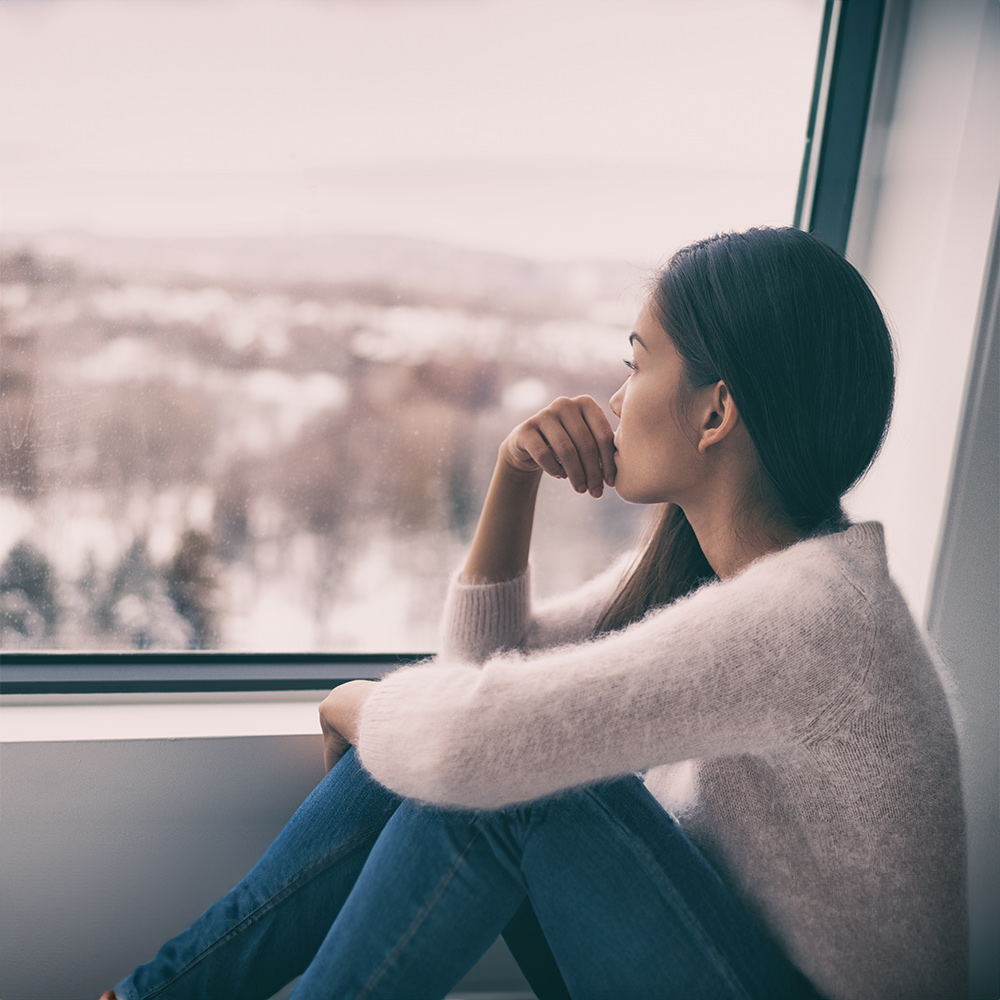 Picture of a depressed woman staring out a window who is in need of depression therapy.