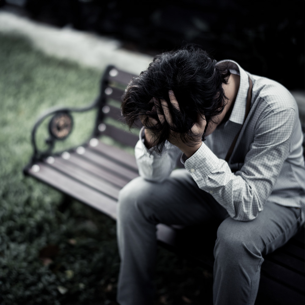 An anxious man bent over and covering face in need of anxiety therapy.